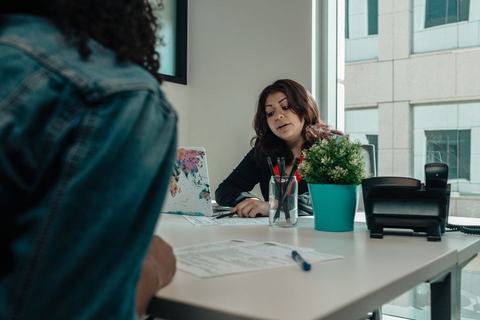 Two people talking across a desk in a small office, paperwork between them