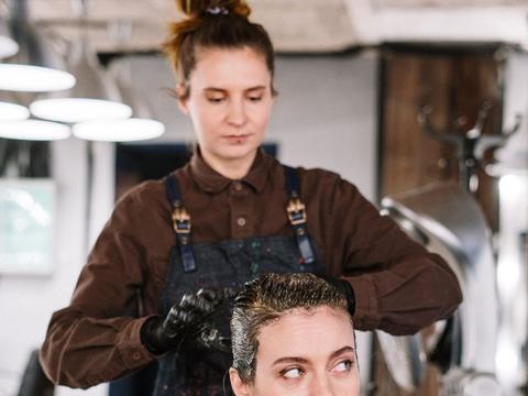 A stylist working color through a client's hair in a salon chair